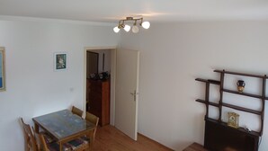 Una habitación con una mesa de comedor de madera, sillas, un pequeño estante con adornos y una puerta que da a otra habitación.