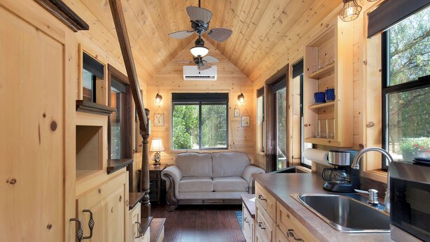 Een knus houten cabin met een kitchenette, een bank en een plafondventilator.
