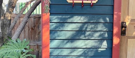 A blue door with a red trim, a wooden fence, and a tree.