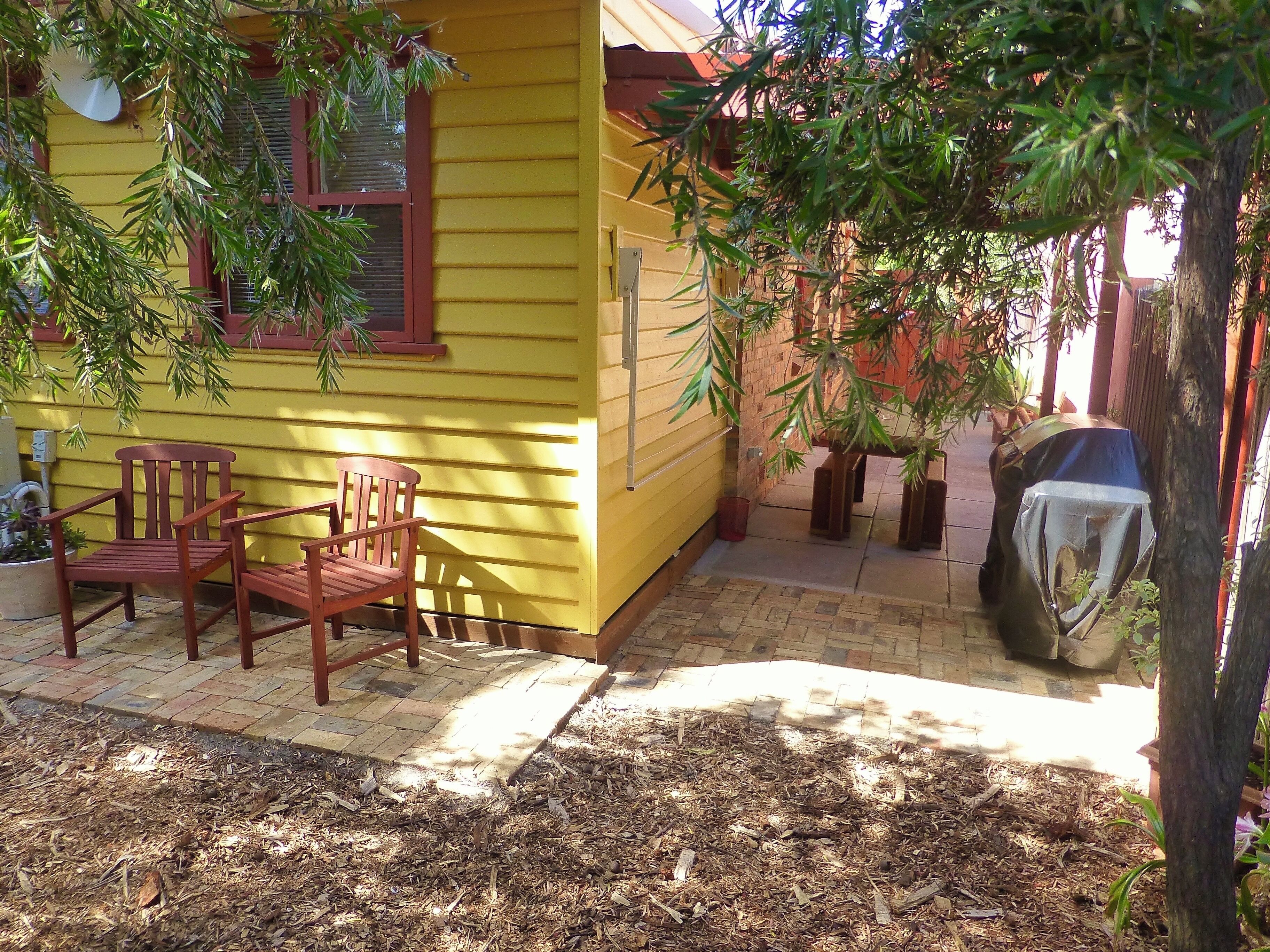 A yellow house with a patio area featuring two wooden chairs and a covered grill.
