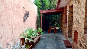 Un patio estrecho con pared de ladrillo, un banco de madera y plantas en macetas.
