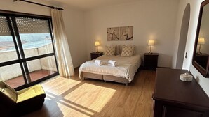 Une chambre d’hôtel avec un lit, deux tables de chevet avec des lampes, un plancher en bois, une fenêtre avec des stores et une vue sur l’extérieur.