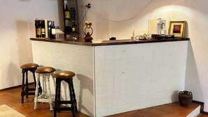 Une cuisine avec un mur recouvert de briques blanches, un comptoir-bar en bois et trois tabourets de bar. Des lampes suspendues sont fixées au-dessus du comptoir, et une machine à café est posée sur celui-ci.