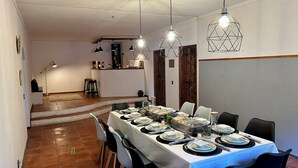 Un espace repas avec une longue table dressée pour le repas, une cuisine en arrière-plan et un escalier menant à un autre niveau.