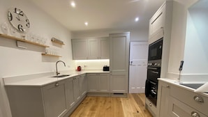 A modern kitchen with grey cabinets, a wooden floor, a built-in oven, and a clock on the wall. - Cosy holiday cottage in the National Park with stunning views and new kitchen. (Widecombe in the moor)