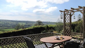 A wooden pergola with a table and chairs, overlooking a scenic valley. - Cosy holiday cottage in the National Park with stunning views and new kitchen. (Widecombe in the moor)