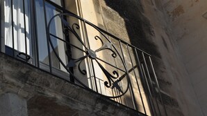 A metal balcony railing with intricate designs, a window with vertical blinds, and a building facade with visible wear and discoloration. - Beautiful, romantic and central (Lecce)