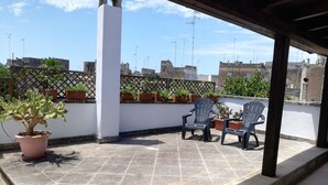 A rooftop terrace with potted plants, two plastic chairs, and a white column. - Beautiful, romantic and central (Lecce)