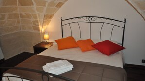A bed with an arched stone ceiling, a nightstand with a lamp, and a neatly folded towel on the bed. - Beautiful, romantic and central (Lecce)
