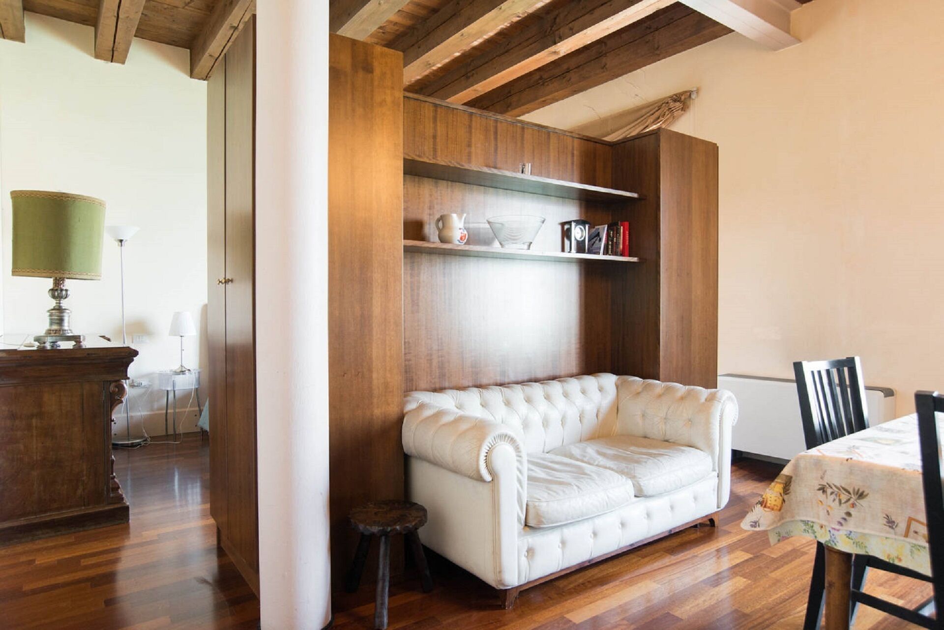 Una sala de estar acogedora con un sofá blanco, vigas de madera, una mesita y una estantería.