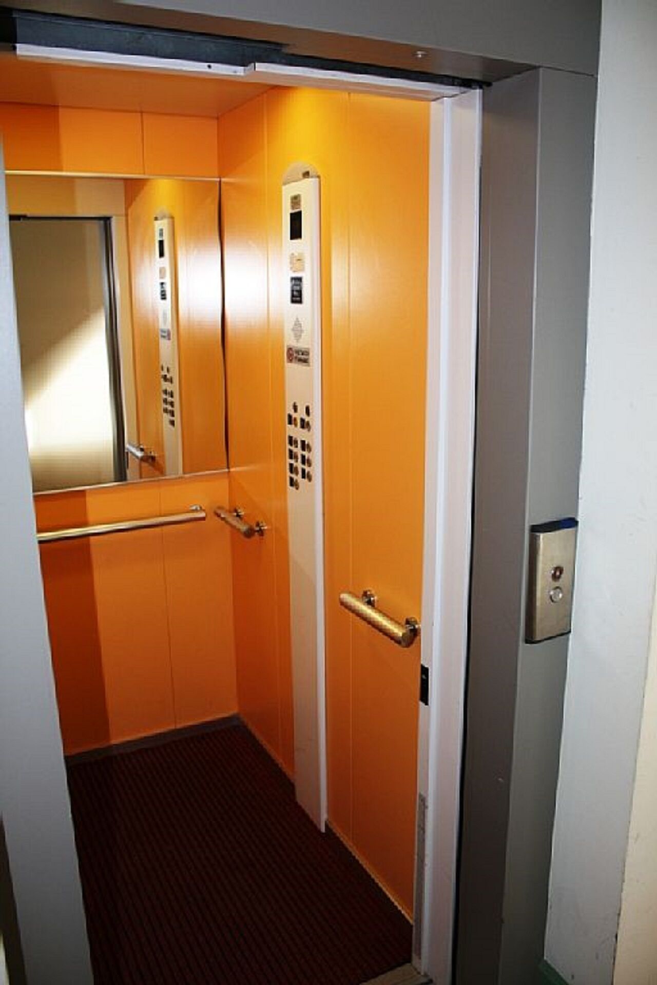 An elevator with orange walls, a control panel, and a handrail.