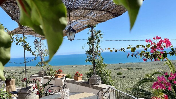Une terrasse extérieure avec une table et des chaises, une lanterne suspendue et une vue sur la mer.