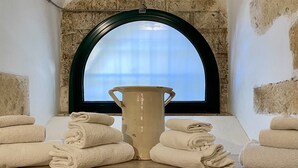 Une salle de bain dotée d’une grande fenêtre en arc de cercle, d’un vase beige et de serviettes soigneusement pliées sur un comptoir recouvert de carreaux jaunes.