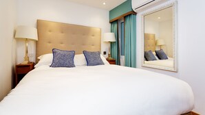 A hotel room with a large bed, two bedside tables with lamps, a large mirror, and an air conditioning unit. - Chelsea Artist's Studio, by Veeve (London)