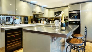 A modern kitchen with stainless steel appliances, a wine bottle, and two wooden bar stools. - Chelsea Artist's Studio, by Veeve (London)