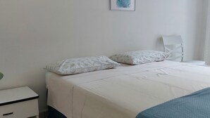 Une chambre à coucher comprenant un lit, une table de chevet, une chaise et deux œuvres d’art encadrées accrochées au mur.