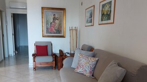 Un salon avec un canapé beige, une chaise en bois avec un coussin rouge et un tableau accroché au mur.