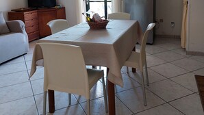 Un coin repas avec une table dressée pour quatre personnes, un réfrigérateur, un téléviseur et un canapé.