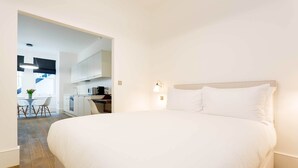 A modern hotel room with a large bed, a small kitchenette, and a dining area with a table and chairs. - Contemporary in Swiss Cottage, by Veeve (London)