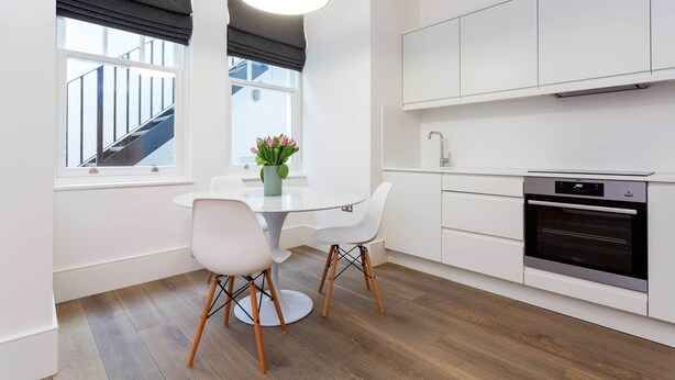 A modern kitchen with white cabinetry, a built-in oven, and a dining area with a round table and two chairs. - Contemporary in Swiss Cottage, by Veeve (London)