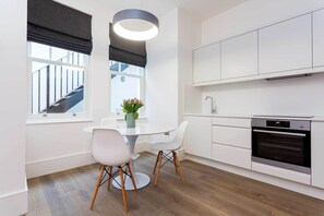Et moderne køkken med hvide skabe, en indbygget ovn og et spiseområde med et rundt bord og to stole.