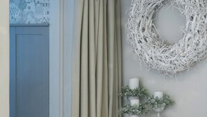 Ett rum med en blå dörr, beige gardiner, en vit krans på väggen och två vita ljusstakar med ljus.