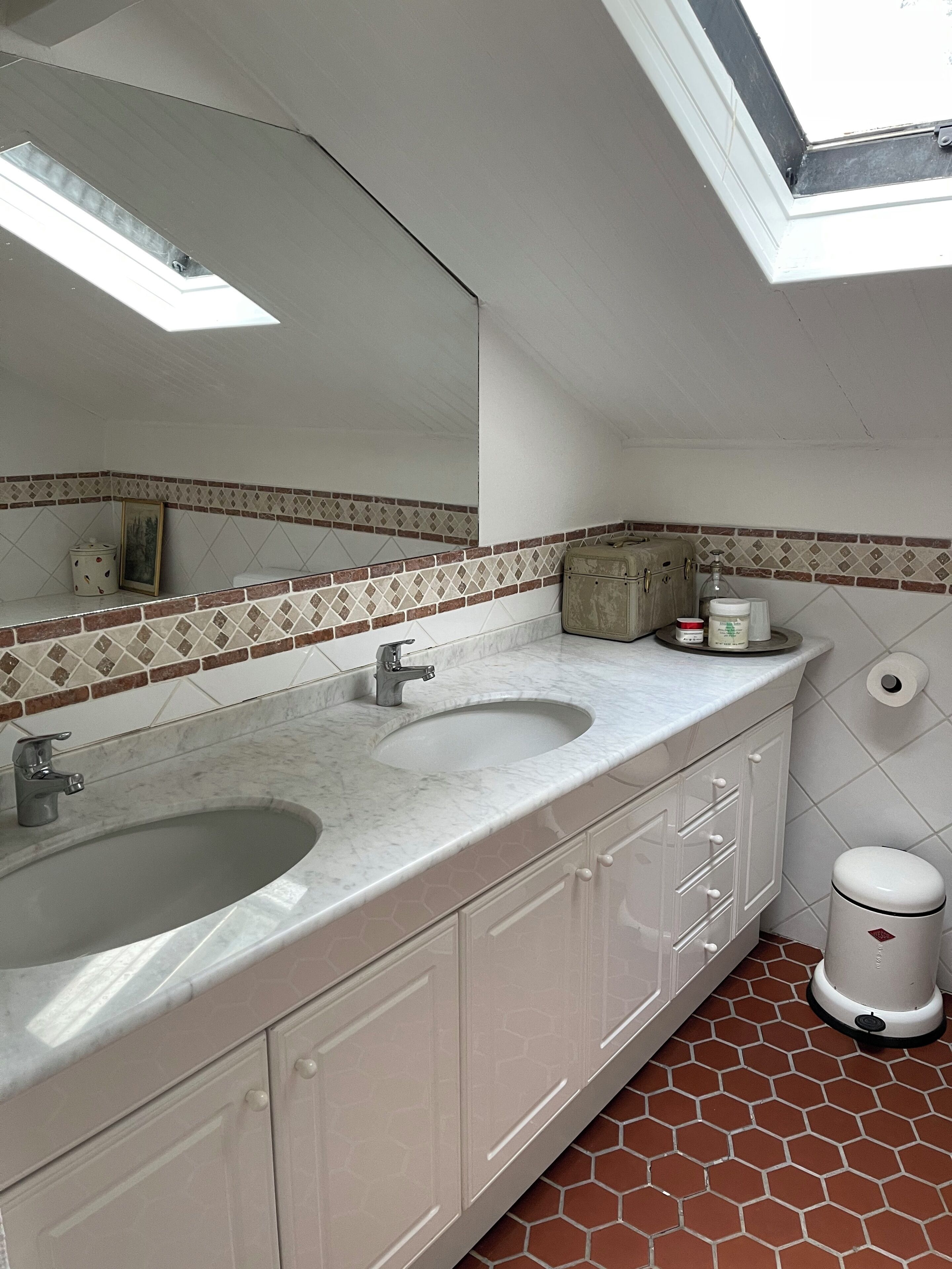 A bathroom with two sinks, a mirror, a towel rack, and a waste bin.