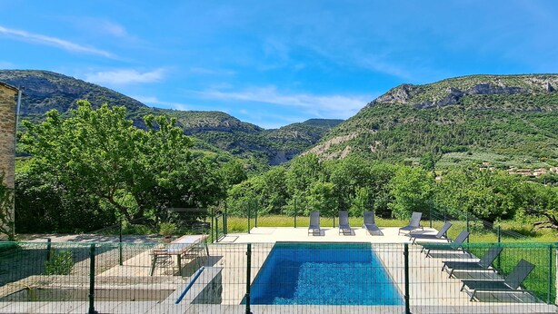 Piscina con vista a montañas, rodeada por una valla y sillas de descanso.