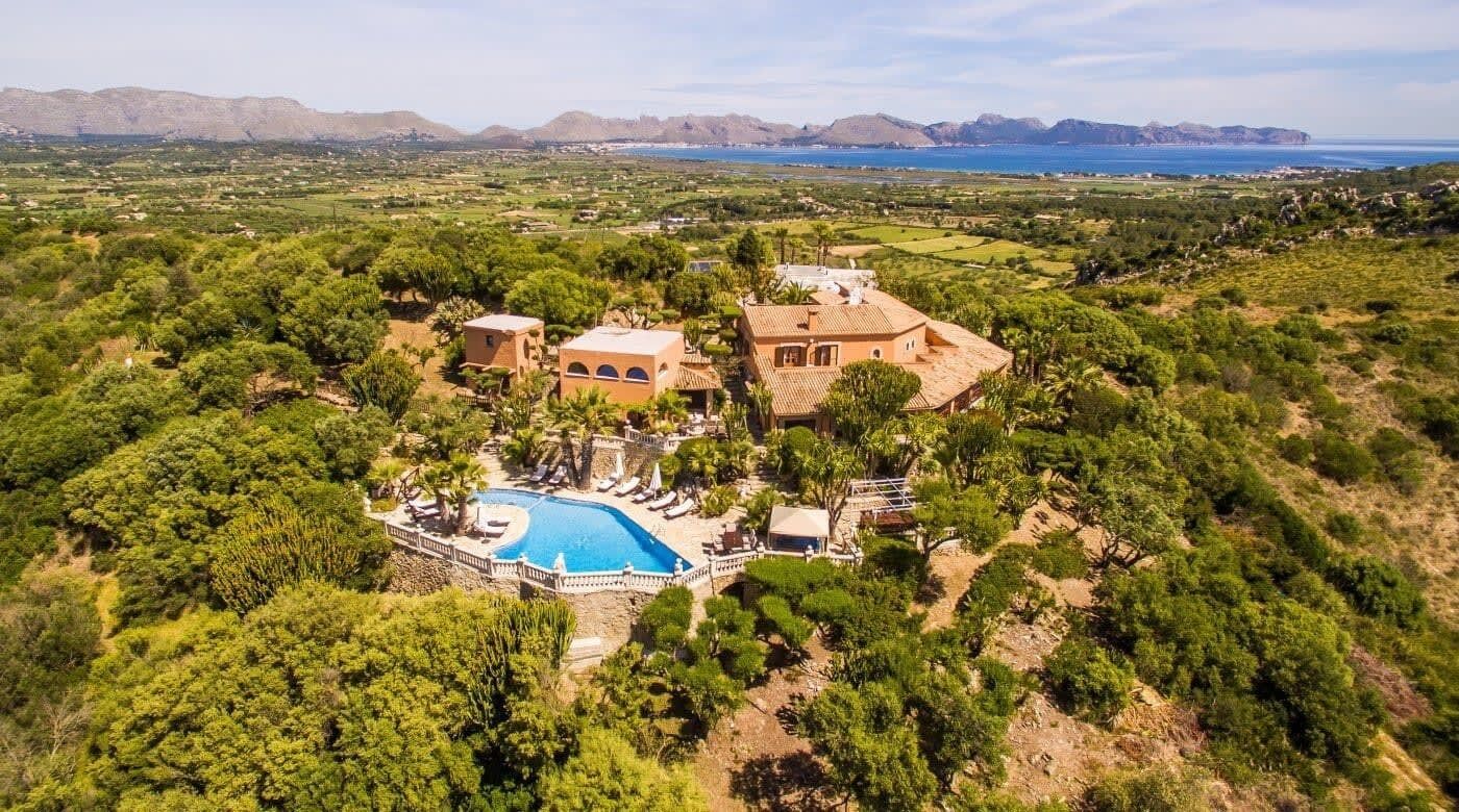 A villa with a swimming pool surrounded by lush greenery and a view of the sea.