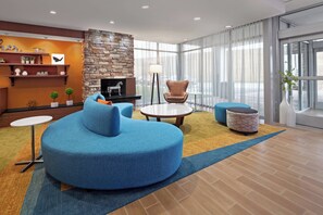 A modern lounge area with a stone fireplace, blue seating, a round coffee table, and a large window offering a view. - Fairfield Inn & Suites by Marriott Poplar Bluff (Poplar Bluff)