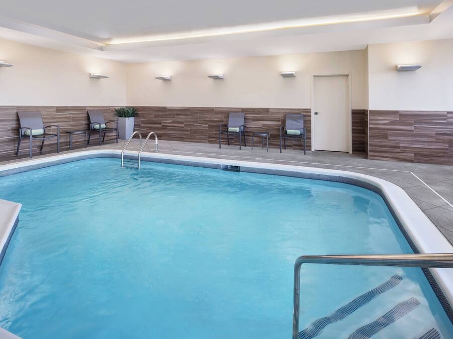 A swimming pool with a tiled deck, surrounded by lounge chairs and a wall with built-in lighting.