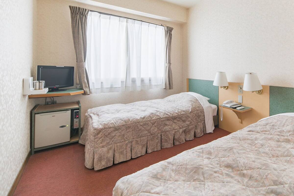 A hotel room with two beds, a desk with a computer, a telephone, and a window with curtains.