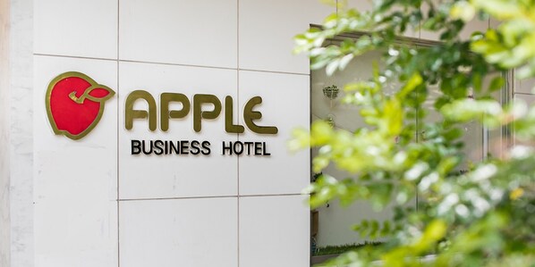 A sign for the Apple Business Hotel with a red apple logo and the name in gold letters. - Business Hotel Apple (Nagoya)