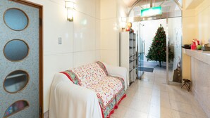 A hotel lobby with a reception desk, a Christmas tree, and a sofa with a colorful blanket. - Business Hotel Apple (Nagoya)