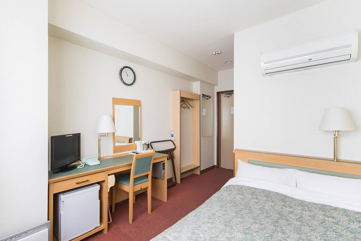 A hotel room with a bed, desk, chair, television, and a small refrigerator.