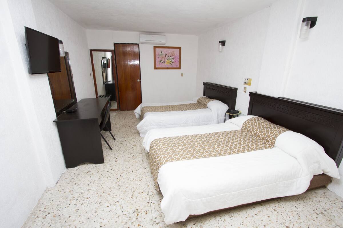 Habitación de hotel con dos camas, un escritorio, un televisor de pantalla plana y una puerta que da a otra habitación.