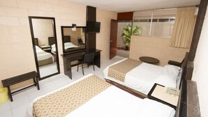 Habitación de hotel con dos camas, un escritorio, una silla, un espejo, una ventana con cortinas y una planta en maceta.