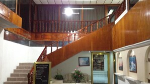 Un vestíbulo de hotel con una escalera de madera, una recepción y un cartel que enumera los servicios.