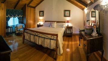 Um quarto aconchegante com teto de madeira, uma cama grande, duas mesas de cabeceira com luminárias, uma poltrona e um penteado.