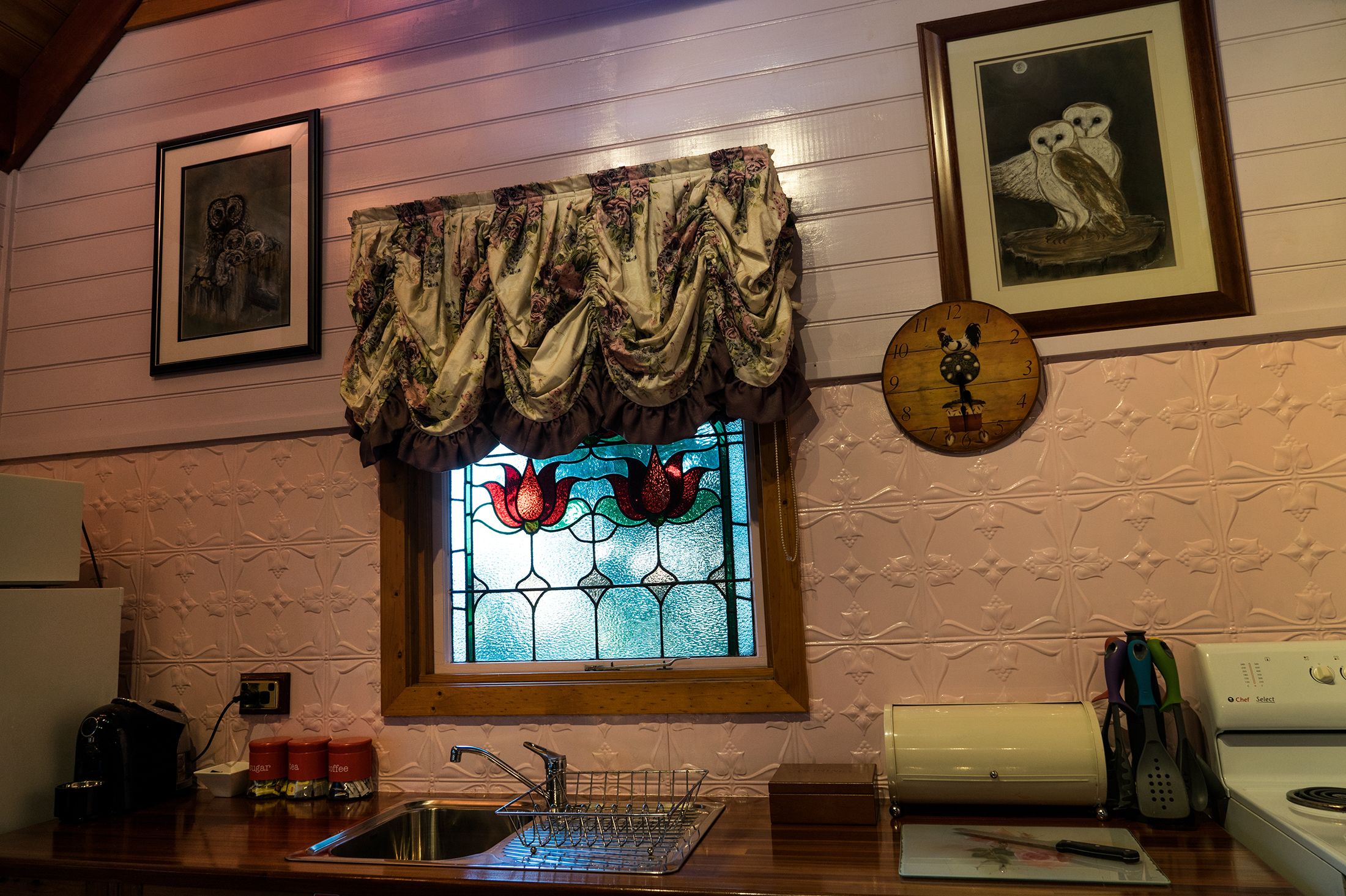 Una cocina con lavamanos, estufa y ventana decorativa con vidrieras.