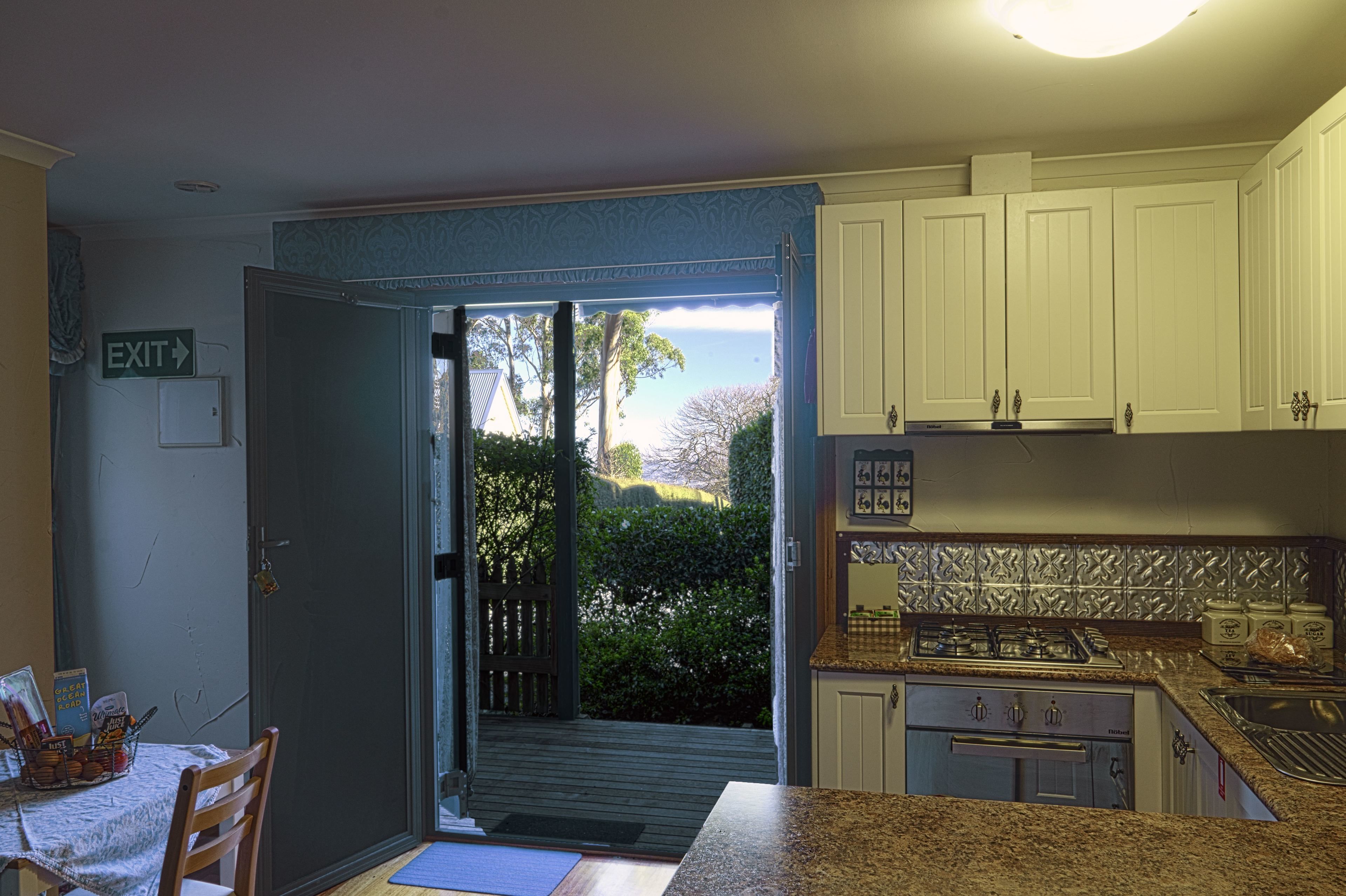 A kitchen with white cabinets, a granite countertop, and a view of the outdoors through an open door.