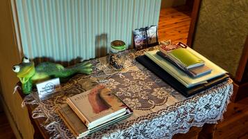 A table with a lace tablecloth, books, a jar with a lid, a frog figurine, and a sign.