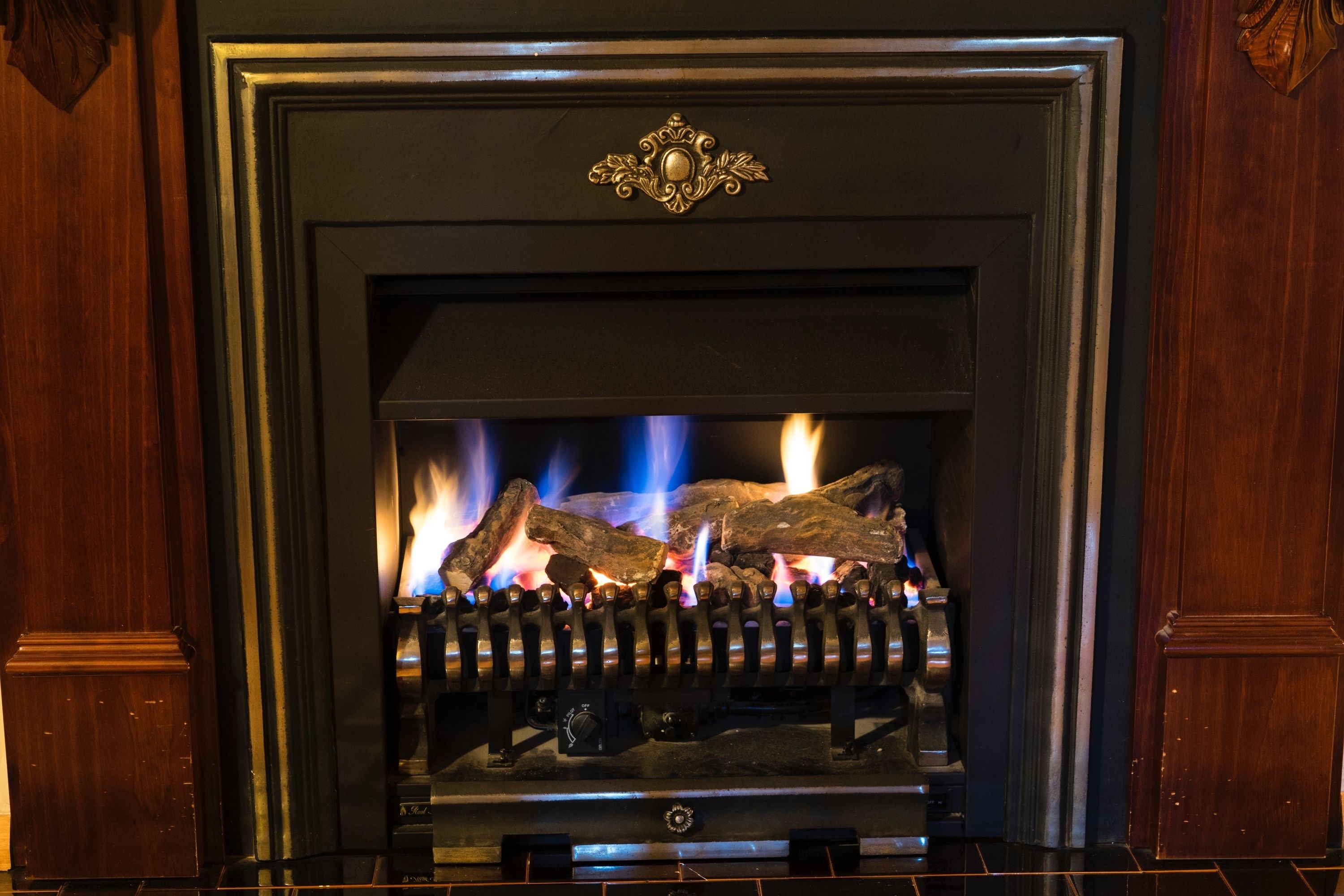 A fireplace with logs burning, a metal grate, and a decorative metal piece above the mantel.