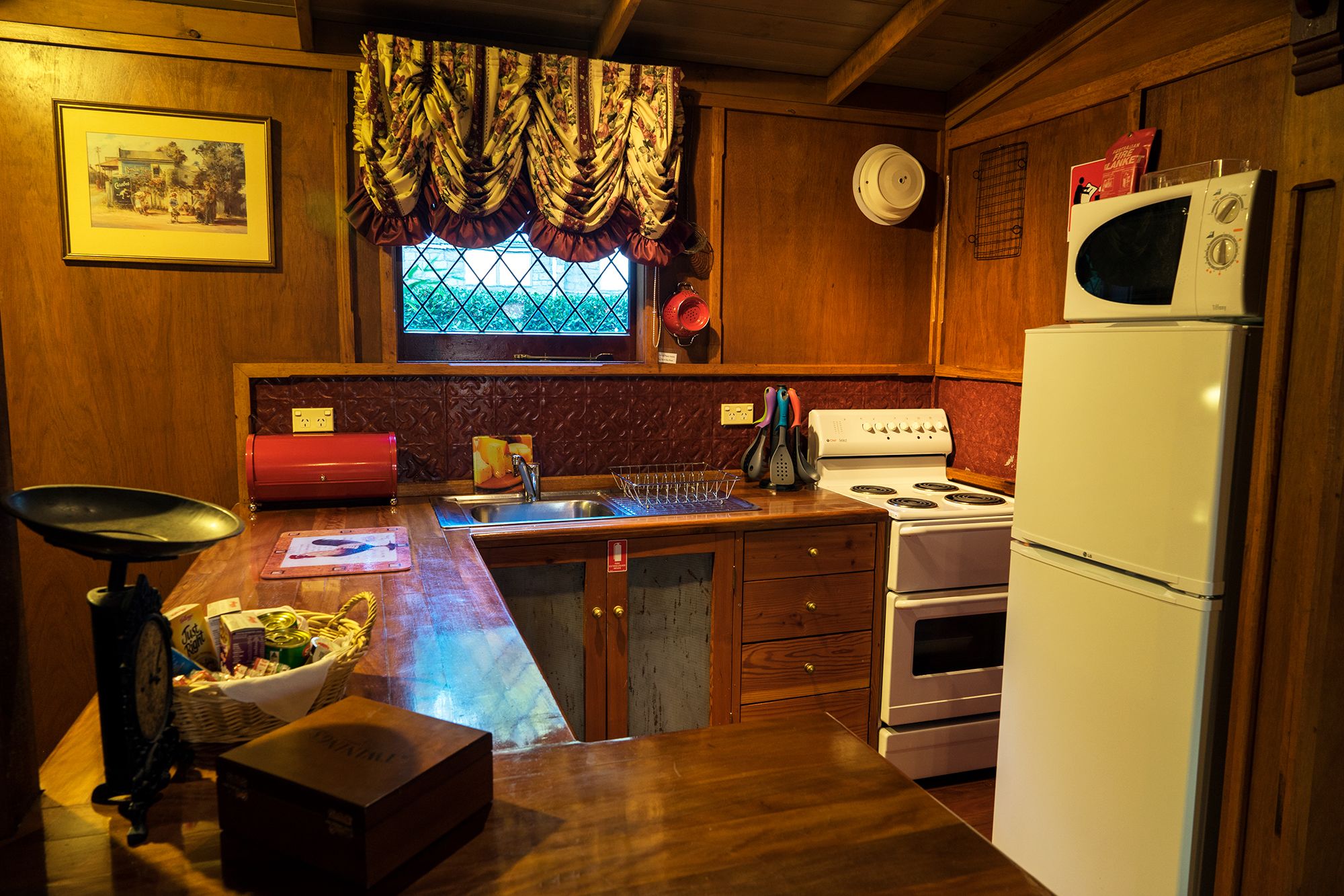 A kitchen with wooden cabinets, a stove, a refrigerator, a sink, and a window with a floral curtain.