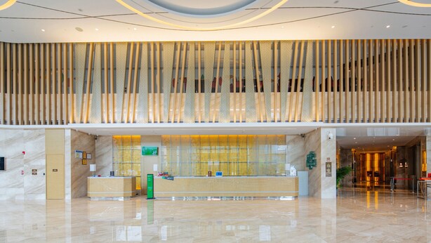A modern hotel lobby with a reception desk, a high ceiling with circular lighting, and a polished marble floor. - Holiday Inn Shaoguan Downtown by IHG (Shaoguan)