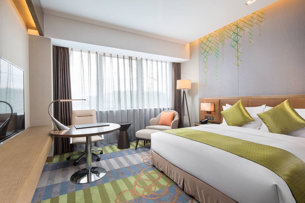A hotel room with a large bed, a desk, a chair, a TV, and a window with curtains.