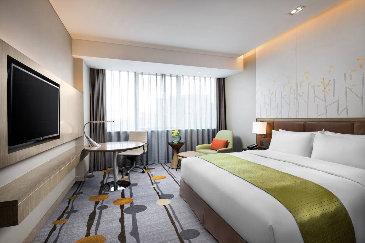 A hotel room with a bed, a desk, a TV, and a window with curtains.