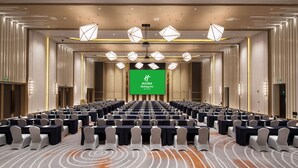 Une salle de conférence avec des rangées de tables et de chaises, un grand écran à l’avant et un éclairage moderne.
