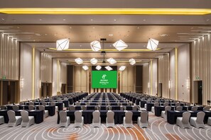 A conference room with rows of tables and chairs, a large screen at the front, and modern lighting fixtures. - Holiday Inn Shaoguan Downtown by IHG (Shaoguan)