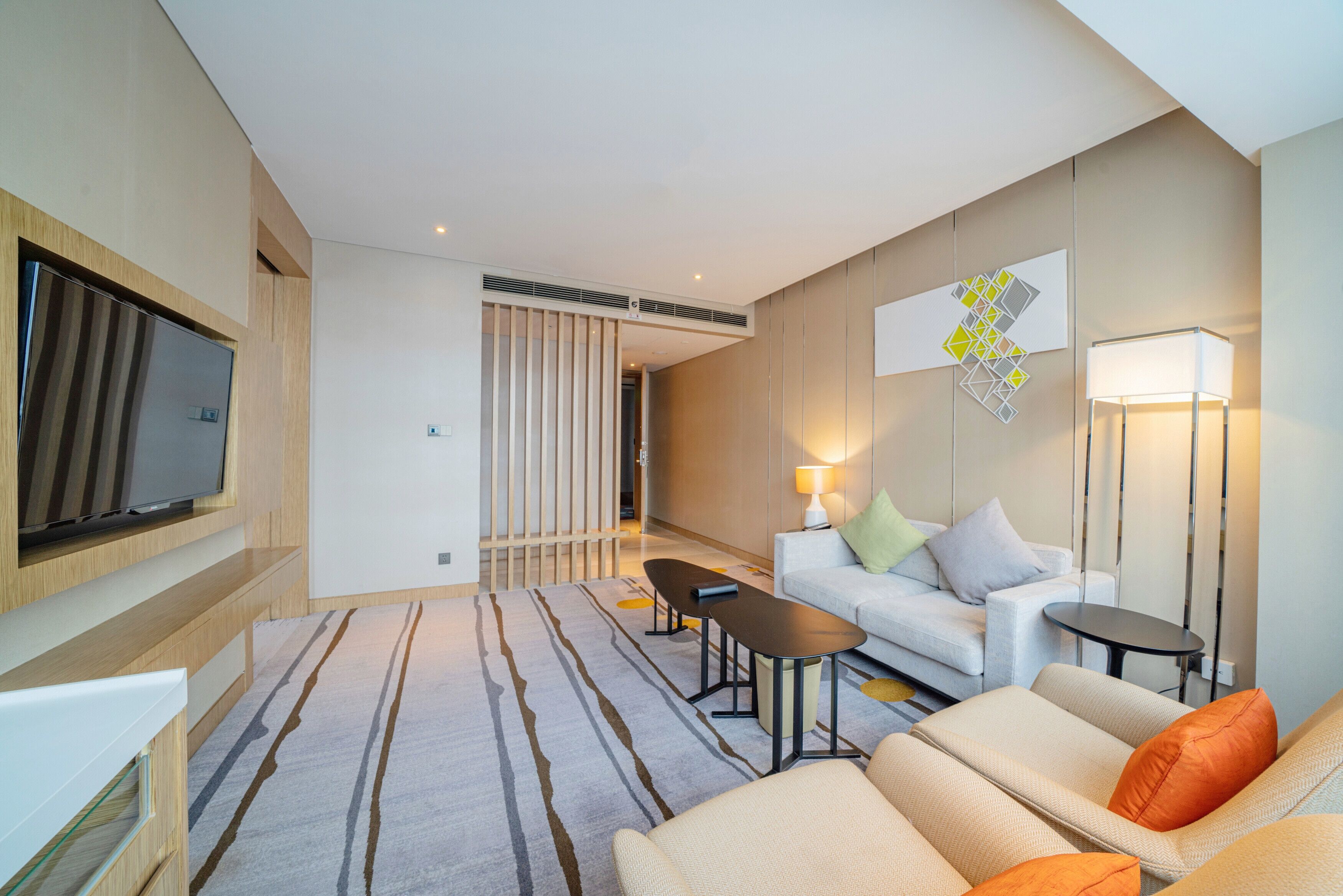Een moderne hotelkamer met een flatscreen televisie aan de muur, een zithoek, een bijzettafeltje en een vloerlamp.